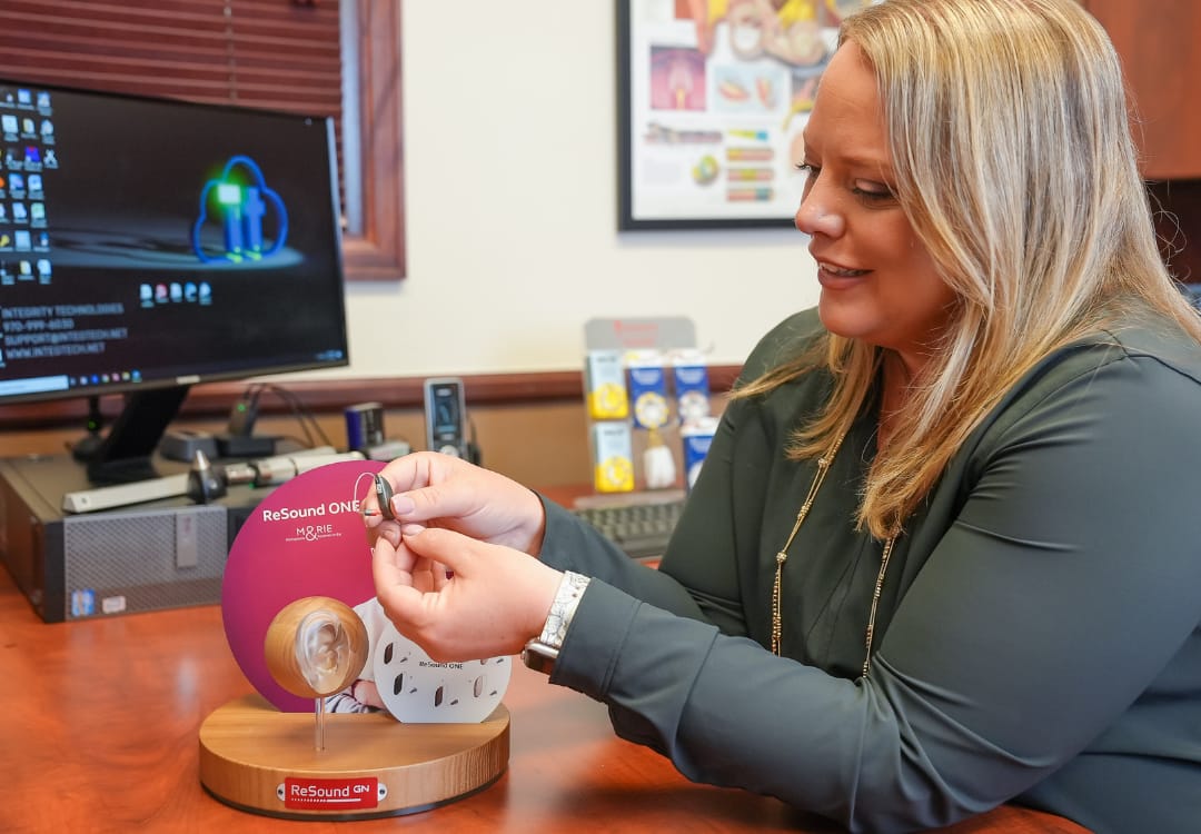 woman-audiologist-holding-a-hearing-aid woman audiologist showing a patient a hearing aid