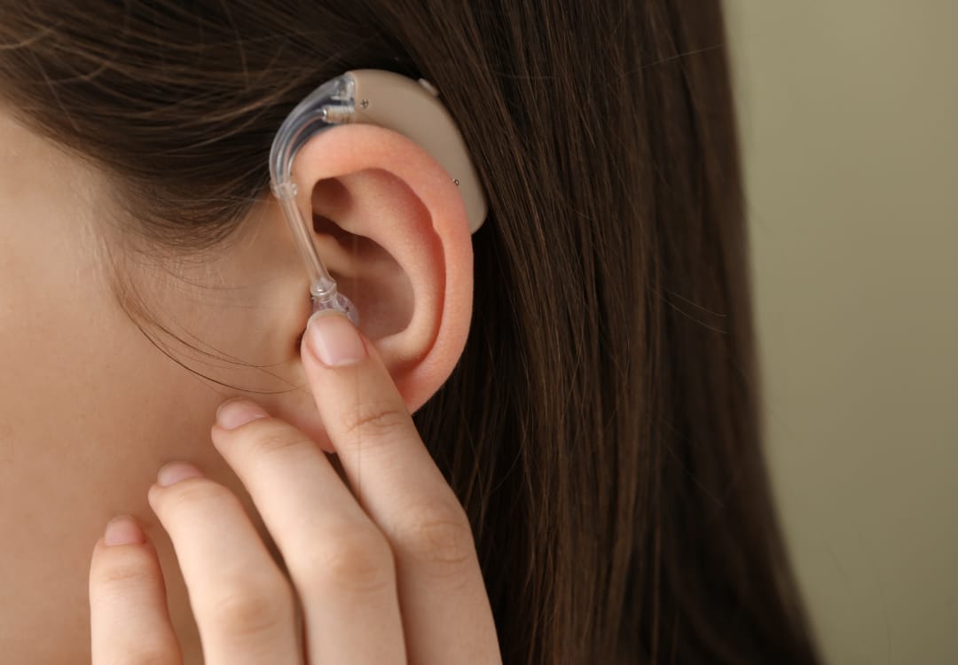 close up of person wearing a hearing aid, touching their ear